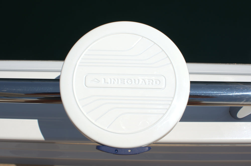 Close-up of the white LINEGUARD unit mounted on a boat's stainless steel rail, with the LINEGUARD name embossed across its circular housing.