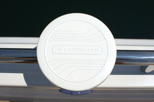 Close-up of the white LINEGUARD unit mounted on a boat's stainless steel rail, with the LINEGUARD name embossed across its circular housing.