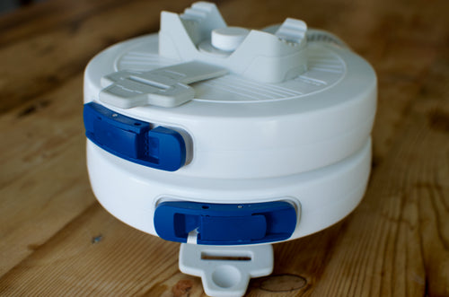 Two stacked LINEGUARD units on a wooden table seen from above at an angle, showing the grey silicone mounting strap and rail cradle on the top unit.