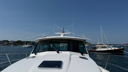 Bow-on view of a white powerboat moored in a harbor with LINEGUARD webbing run across the hardtop between the two antennas, held at each end by an Antenna Mate.