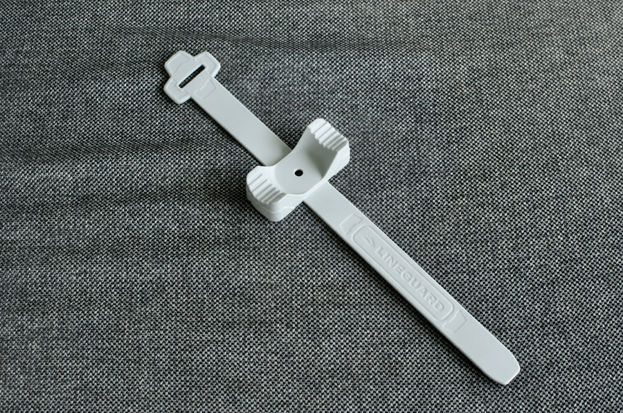 A single white QUIK-Strap XL laid on grey fabric, showing the long ribbed silicone tail with the LINEGUARD name embossed along it and the ridged cradle at its centre that seats against the rail.